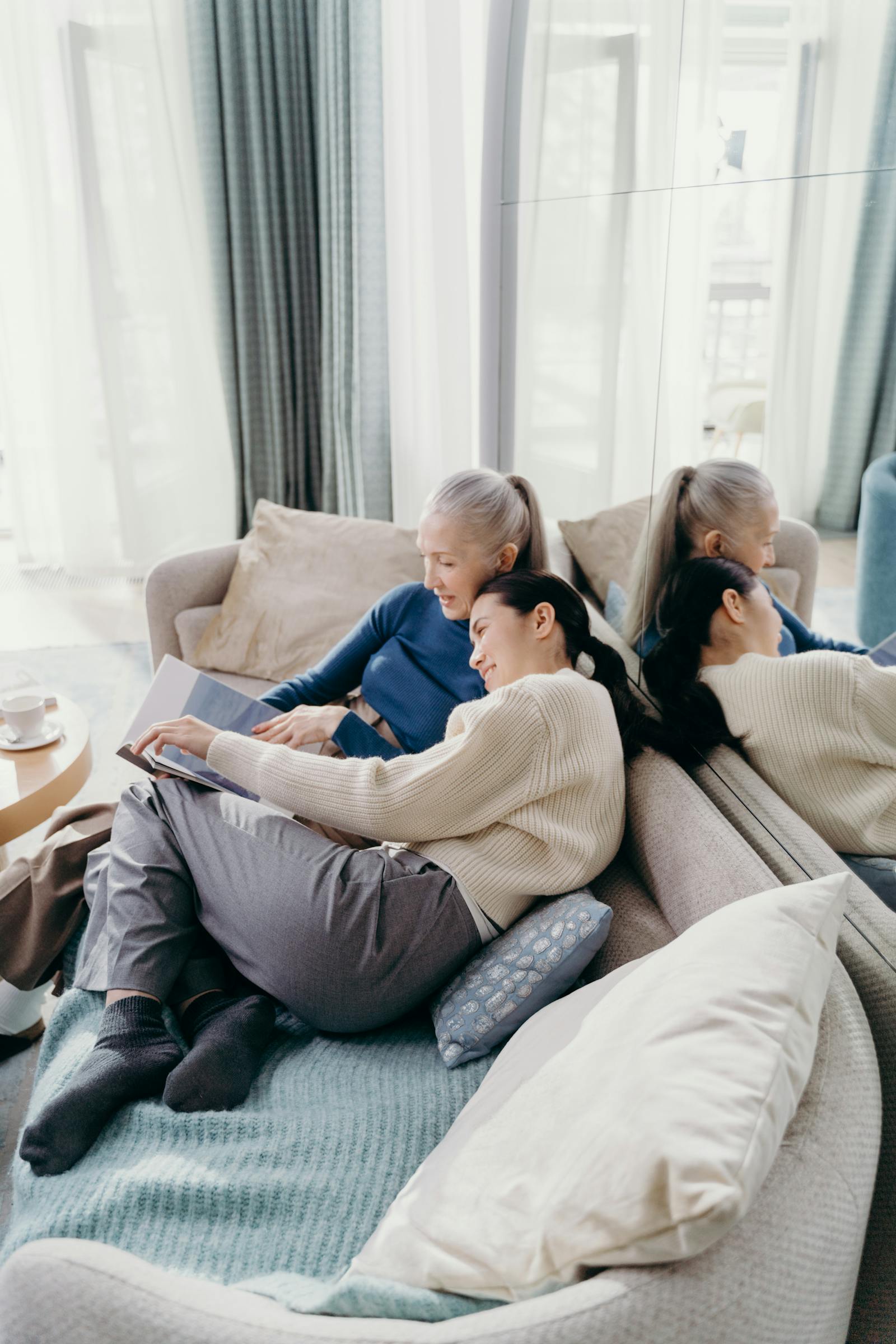 A mother and adult daughter sitting close together with a photo album on the couch.
